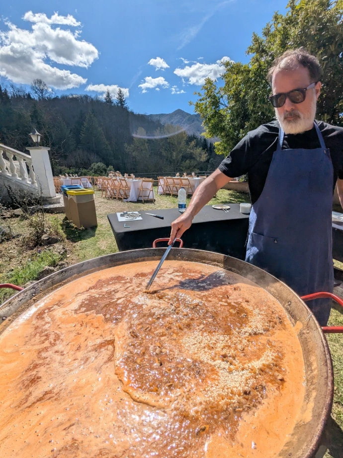 Cocinero removiendo una paella gigante en el jardín de una boda, con las mesas montadas detrás