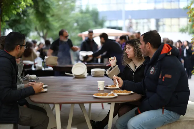 Convidats menjant paella al voltant d'una taula de fusta