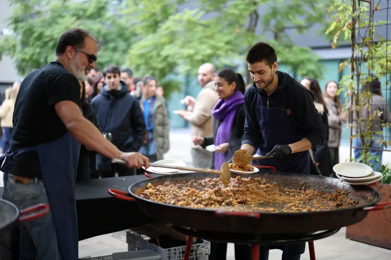 Dos cuiners servint paella a una cua de convidats en un jardí
